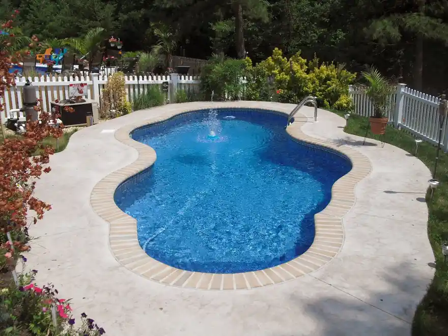 Freeform vinyl pool with a fountain jet running, framed by a white picket fence