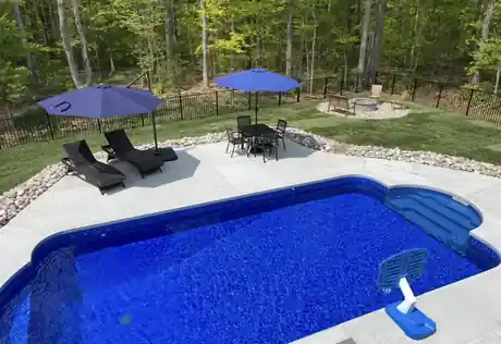 Rectangular pool with a patterned blue liner, concrete deck, two umbrellas and a fire pit