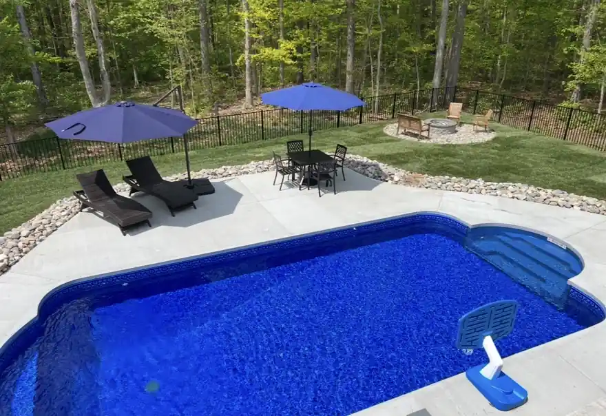 Rectangular pool with a patterned blue liner, concrete deck, two umbrellas and a fire pit
