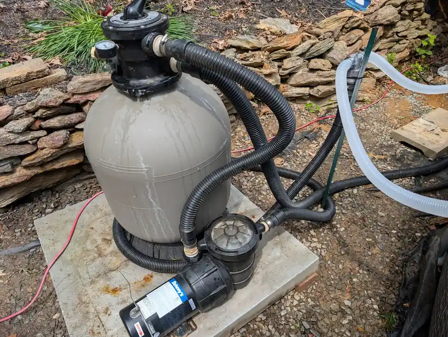 Sand filter and pump plumbed on a concrete pad beside an above ground pool