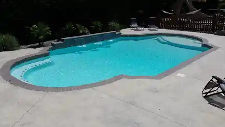 Freeform pool with an aqua finish, a tile band and a row of spill jets on a stamped concrete deck