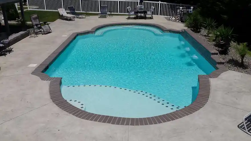 Bright freeform pool with a brick-red tile band and a broad concrete deck