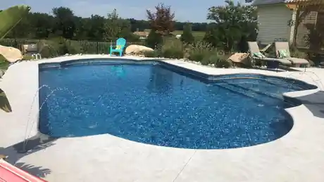 Blue pool edged with boulders and a flagstone deck, with an Adirondack chair and lounge seating
