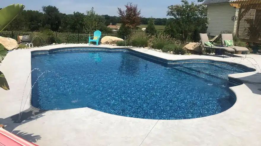 Blue pool edged with boulders and a flagstone deck, Adirondack chair and lounge seating