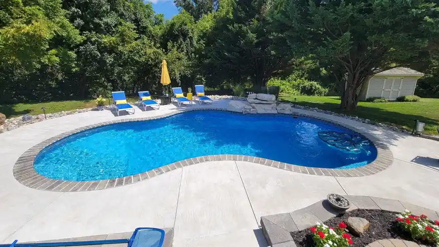 Freeform pool with a brick-red tile band and a row of blue loungers on the deck