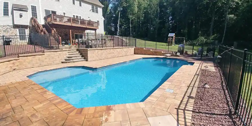 Rectangular pool with a tan paver deck, stone steps and a black aluminum fence