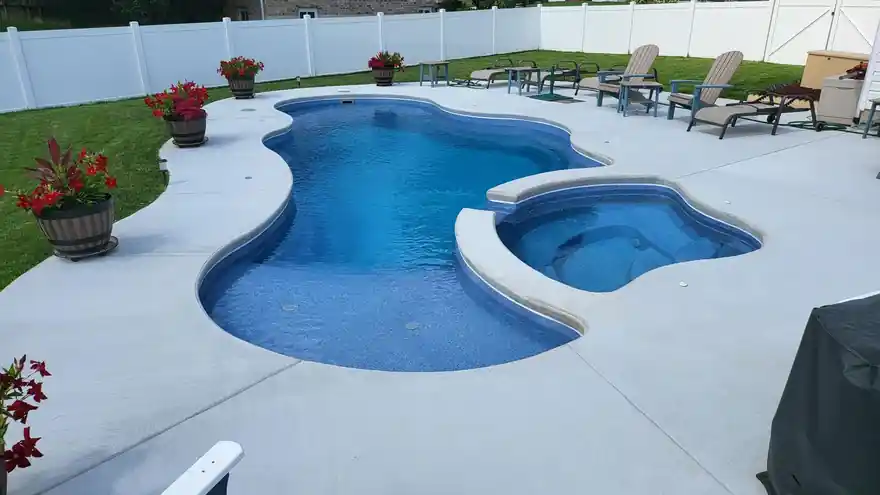 Raised round spa beside a freeform pool on a broom-finish concrete deck