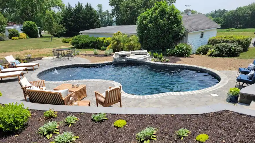 Freeform in-ground pool with a stacked-rock waterfall, flagstone patio and teak seating