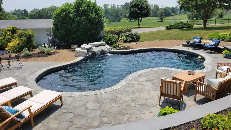 Flagstone deck around a freeform pool with a rock water feature and outdoor sofas