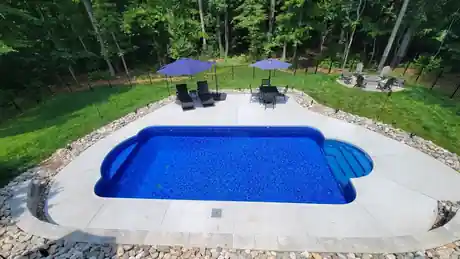 Rectangular vinyl pool with steps set into a wooded lot, gravel border and lawn