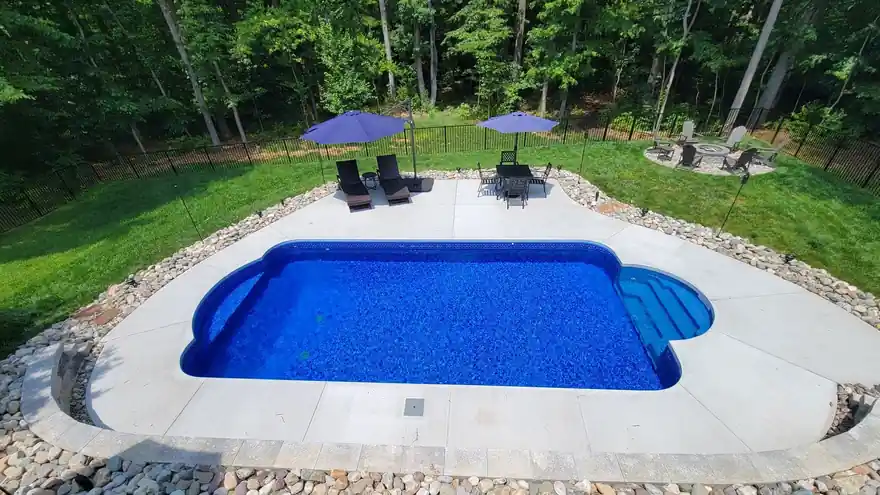 Rectangular vinyl pool with steps set into a wooded lot, gravel border and lawn