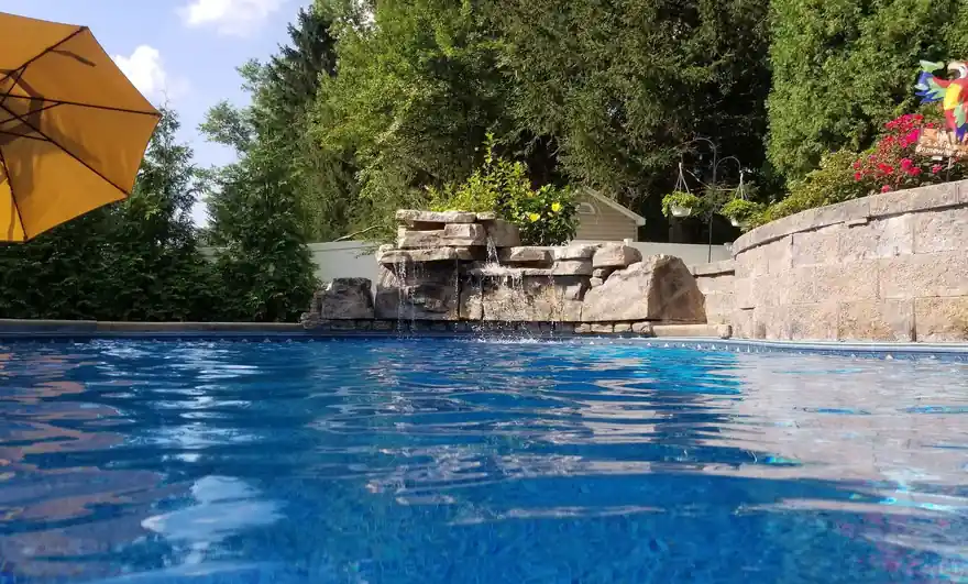 Rock waterfall spilling into a blue pool beside a split-face block retaining wall