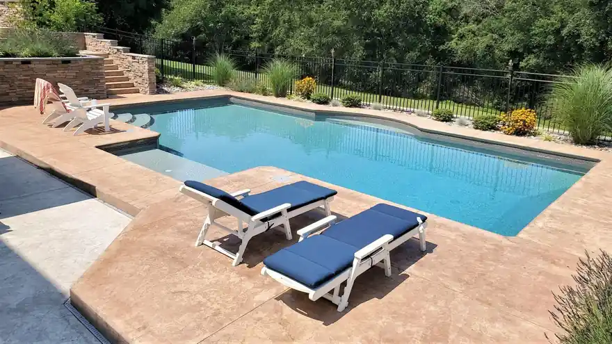 Stamped concrete deck with navy cushioned loungers beside a rectangular pool