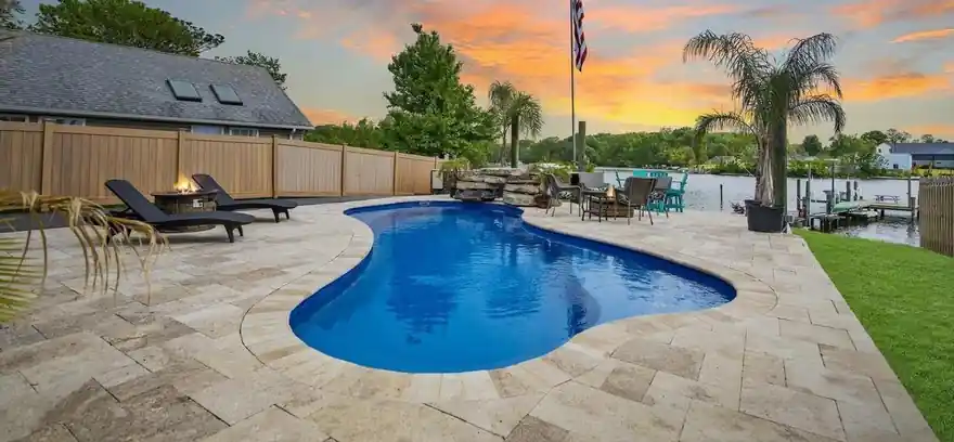 Freeform pool on a large-format paver deck at sunset beside the water